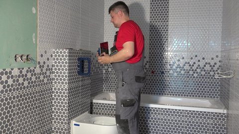 Plumber man mount toilet water flushing button in new apartment bathroom. Static shot.