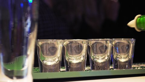 Syrupy brown liquor being poured into a line of shot glasses