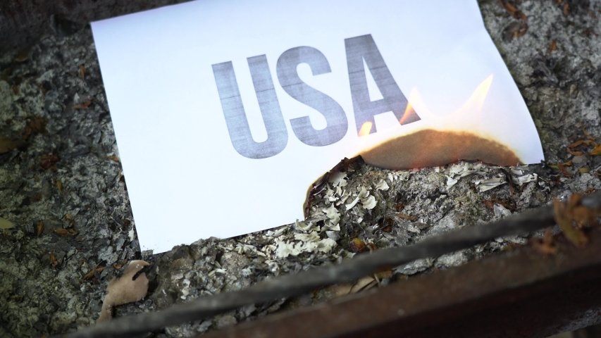 The inscription USA on a white A4 size sheet in the ash. The paper with black word burn, smoke and turns into ashes. The concept of war.