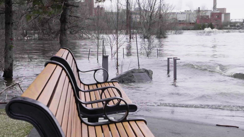 Waves from the Ottawa River flooding roll over walking paths next to a bench in a park