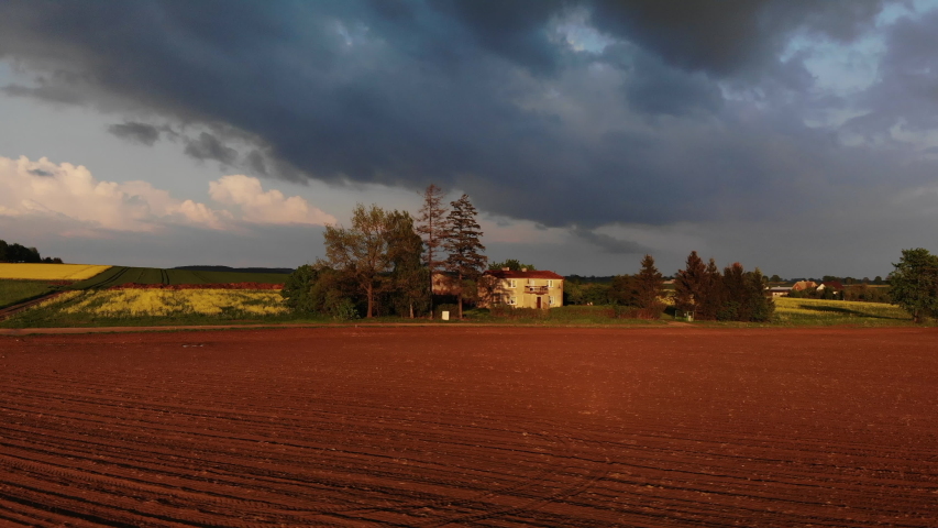 Round drone shot of small cottage in rainy weather at sunset. HDR sunset over the old cabin house with brown field and few trees near by.