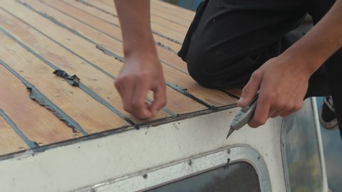 Trimming sika flex mastic flashing sealant at edge of cabin, wooden boat