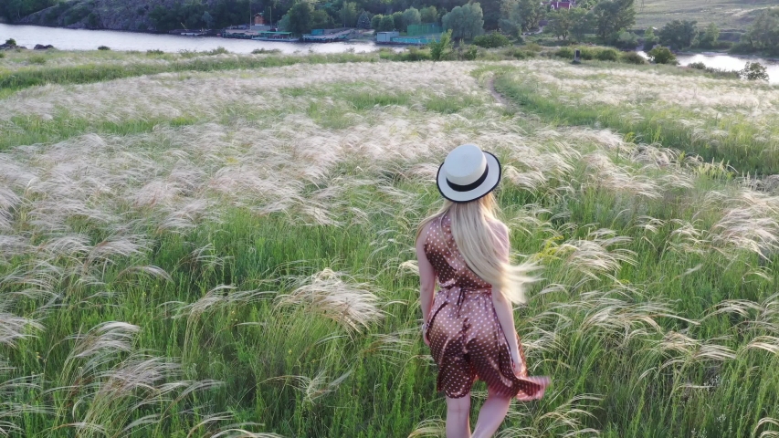 Beautiful girl in dress and hat on the field in the setting sun.