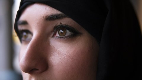 Extreme close-up of a young middle eastern muslim woman in black hijab opening dark brown eyes and looking forward. Blinking in slow motion