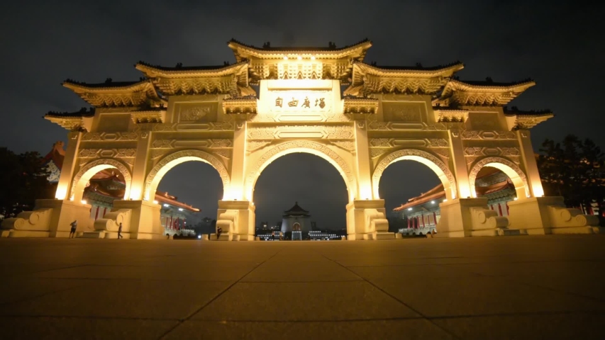 Awesome night view of the Gate of Great Piety at Liberty Square in Taipei, Taiwan. Female tourist crossing the square. The National Chiang Kai-shek Memorial Hall is visible in background.