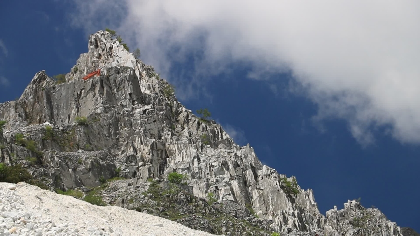 Carrara, Tuscany, Italy. White Carrara marble quarry in the Apuan Alps. A mountain peak near Colonnata with blue sky and clouds.