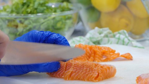 Chef using knife slice raw salmon on chopping board.