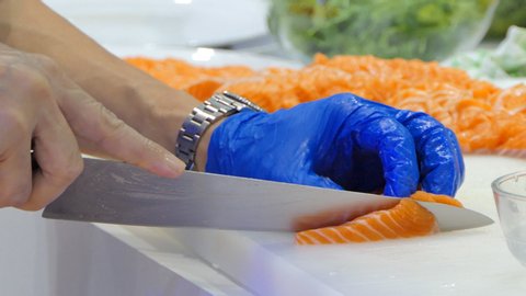 Chef using knife slice raw salmon on chopping board.