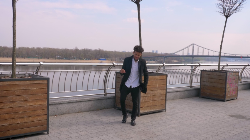Closeup portrait of young happy african american businessman walking dancing looking at camera and smiling cheerfully on the street in the urban city