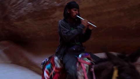 
PETRA, JORDAN - May 2019: Jordanian Bedouin man rides a donkey in Petra, largest monument, UNESCO World Heritage Site, Jordan. The Siq, a narrow stone gallery