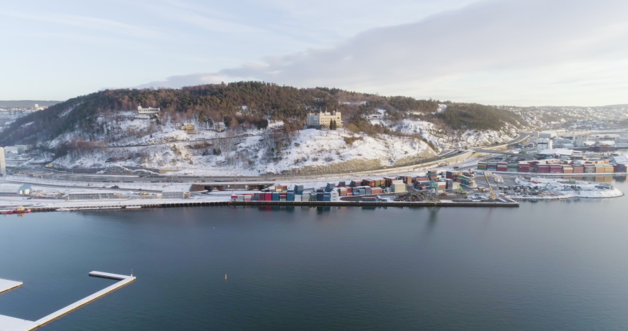 4K aerial with pan motion of the highway to Oslo city center, a maritime container port with cranes and a forest in a colourful winter sunset in Oslo.