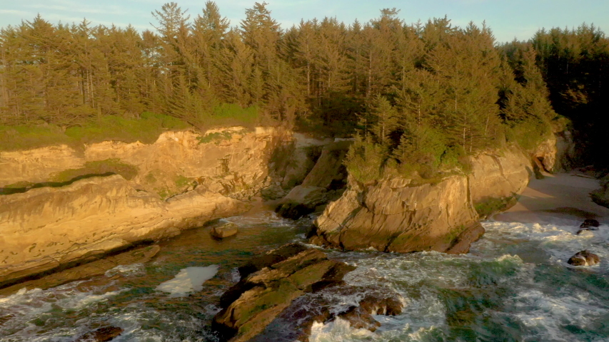 Drone flying backwards over the ocean, revealing dramatic cliffs of Yoakam Point near Coos Bay at wild the Oregon Coast.