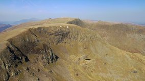 Aerial drone video, downward tilt of UK Lake District mountains beneath blue sky. Ruthwaite Cove and Nethermost Pike, with Helvellyn in background.