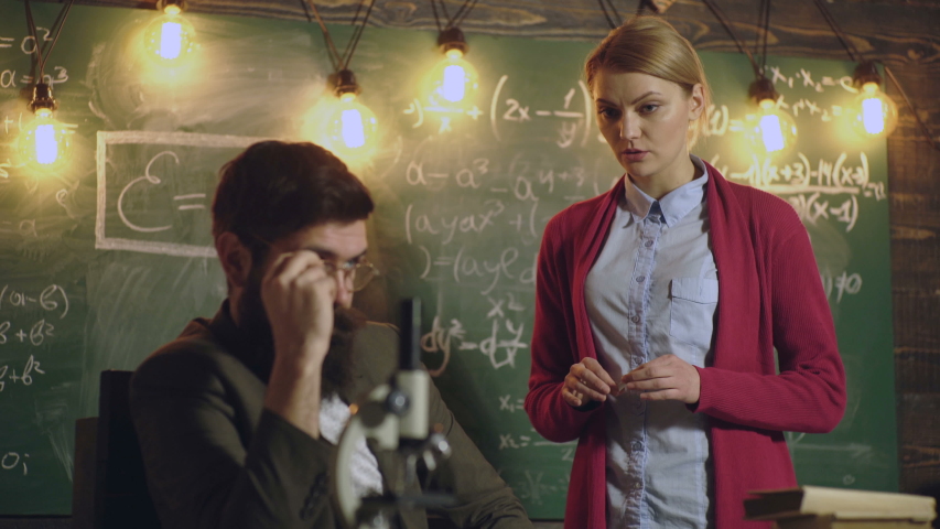 Female student discusses with a bearded teacher in glasses standing near a green school board on which different formulas are written. Sharing International Friend Concept. Back to school. Background Royalty-Free Stock Footage #1030716011