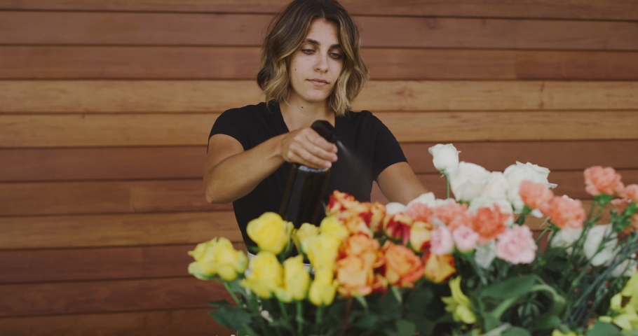 Young florist woman smiling and watering her flowers with water, professional florist preparing flowers