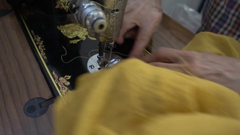 unknown tailor senior woman's hands sewing fabric with an old sewing machine on table