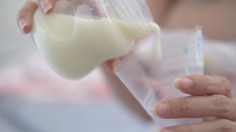 Close up young mother pouring breast milk or mother's milk into breast milk storage bag.