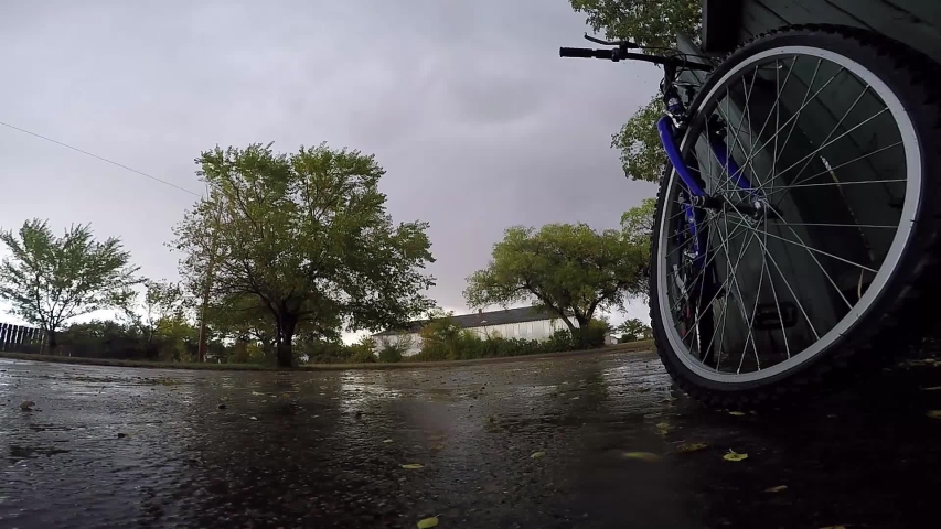 Bike leaning up against a blue wooden fence in the driveway of a house on a rainy day.