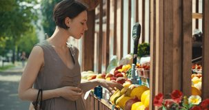 Woman choosing fruits in street kiosk in tourist city center. Girl buying fruits and vegetables at farmers shop. Healthy Food. 4K slow motion raw video footage 60 fps