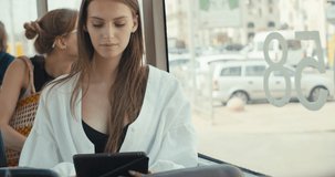 Girl sitting in tram using touchpad for chatting in social networks via free wifi connection, young woman reading e-book on portable pc in public transport. 4K slow motion raw video footage 60 fps