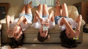 Teenager girls triplet sisters at home watch smart phones in social media lying on couch upside down - Powered by Shutterstock - Get 15% off with code: PIKWIZARD15