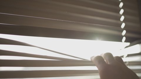 Hand pulling down window blind to peek outside - watching from an office or house room - staying inside safe in home - lonely or curious person or spy looking for mystery hiding in apartment - closeup