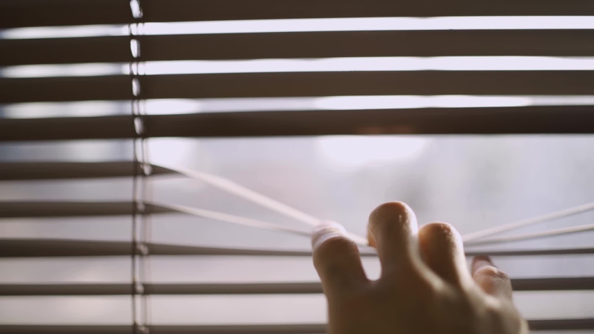 Close up of a hand reaching and opening a crack in the window blinds - looking through the closed shutters in office or house - watching and spying outside - staying home curious or lonely man | Shutterstock HD Video #1030751666