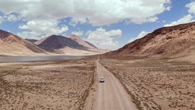 Aerial over off road 4x4 car driving along gravel trail path near arid desert mountains.Pamir Highway silk road trip adventure in Kyrgyzstan and Tajikistan desert,central Asia.4k drone flight video