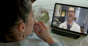Sick woman lying in bed having a telemedicine appointment with a doctor on a laptop computer shaking her head both yes and no while the physician is consulting with her on a video chat