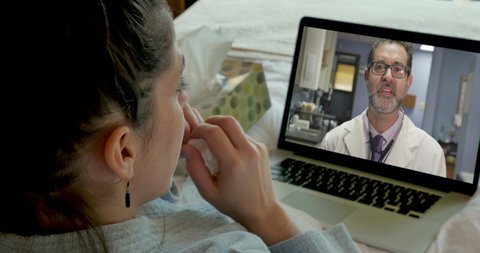 Sick young woman with a laptop computer video chatting with a doctor during a virtual telemedicine appointment in her bedroom