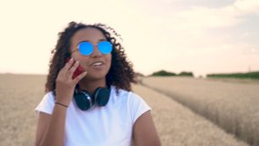 Slow motion follow shot video of beautiful mixed race African American girl teenager young woman in white T-shirt and blue sunglasses walking talking on her mobile cell phone
