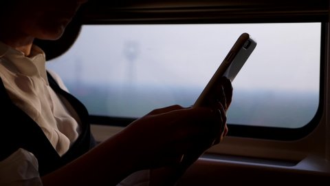 Woman using phone white travel by high speed Beijing–Shanghai train. Slow motion shot, lady hold smartphone and type message, sitting against window, blurred background