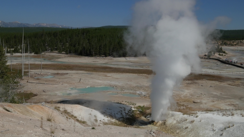 Steaming water streams from a geyser basin and over the rust colored ...