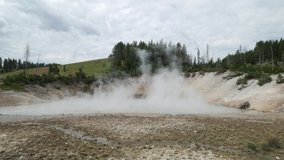 Wide steady shot of steam rising from the mud volcano area at Yellowstone National Park in Wyoming.
