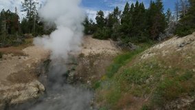 Medium wide steady shot of the Dragon’s Mouth Spring releasing billows of hot steam at Yellowstone National Park in Wyoming.