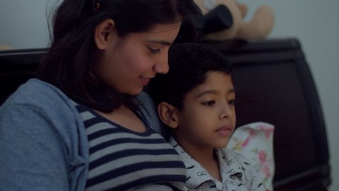 Closeup side shot of young Indian mother and her son spending quality time at bed time. A shot of an Asian mother and son spending time together while watching a movie.