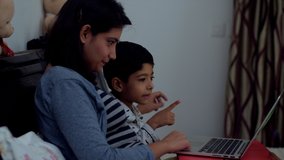 Side shot of an Indian mother and son watching cartoon story movie on the laptop - Technology in your bedroom. Video of a young mother and her 5-year-old son glued to the laptop screen.