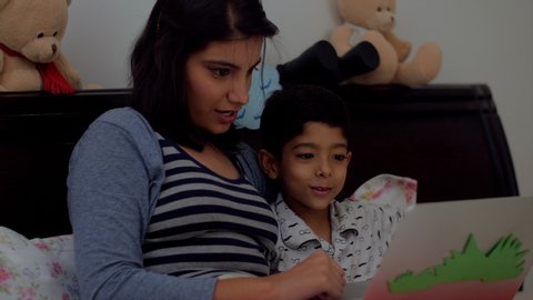 Indian mother and her cute son watching a video on the laptop at bedtime - Spending quality time together. Shot of a happy mother and son watching a cartoon movie on their laptop.