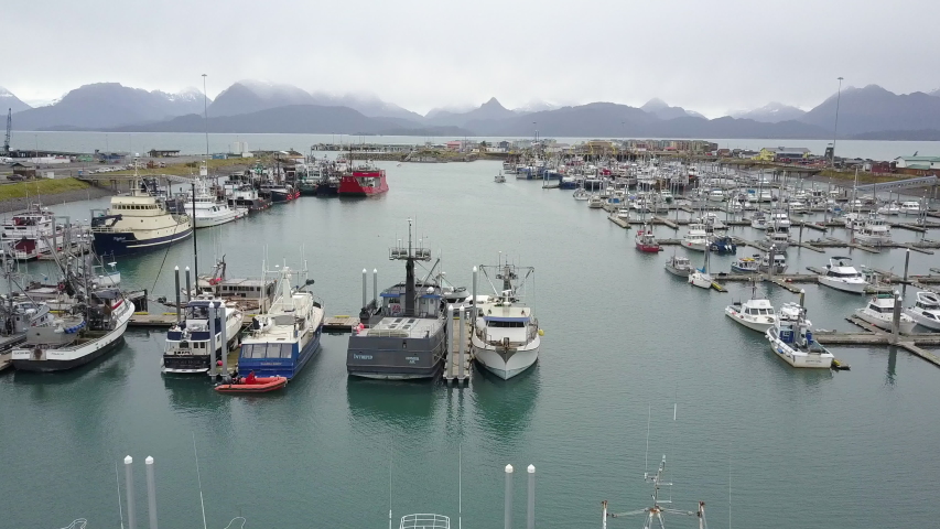 Aerial shot flying over a busy boat harbor in the beautiful small city of Homer, Alaska, with an incredible backdrop in the distance
