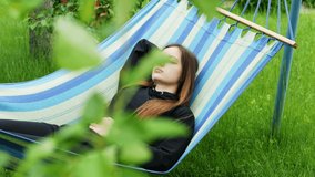 Beautiful young woman sleeping on a hammock in the green garden, resting and dozing in summer day, lifestyle video