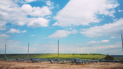 lines on gas and oil pipes on ground at modern refinery complex against green field and pictorial sky timelapse