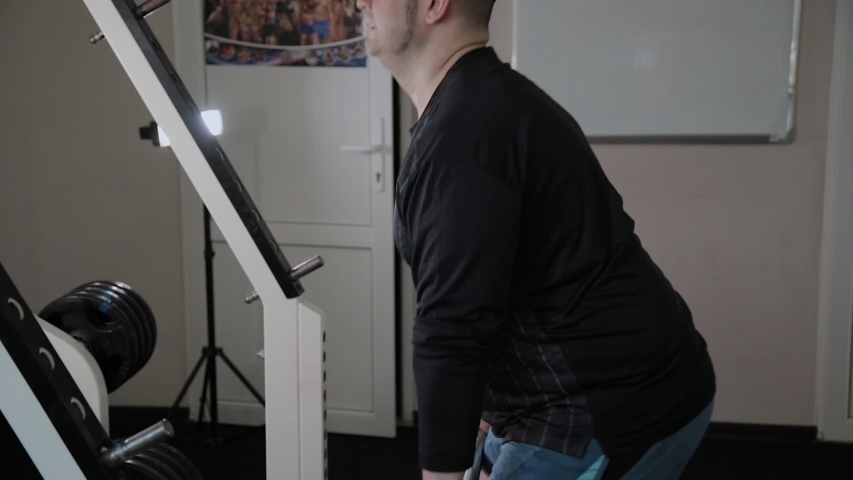 Adult man with overweight performs deadlift in the gym.
