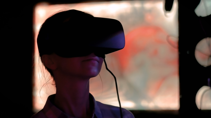 Woman using virtual reality headset and looking around at interactive technology exhibition with changing multi color light illumination. VR, augmented reality, immersive and entertainment concept Royalty-Free Stock Footage #1030802978