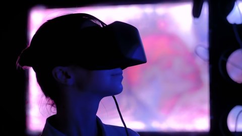 Woman using virtual reality headset and looking around at interactive technology exhibition with changing multi color light illumination. VR, augmented reality, immersive and entertainment concept