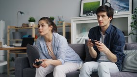 Girl and guy carefree young people are playing video game sitting on sofa expressing positive emotions. Girl is winning celebrating success, guy is losing.