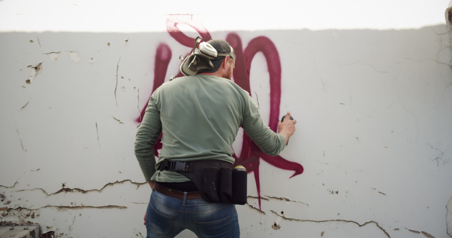 Rear view of Caucasian graffiti artist painting with aerosol spray on the wall. He is creative 