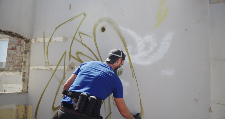 Rear view of Caucasian graffiti artist painting with aerosol spray on the wall. He is wearing protective mask
