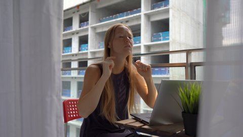 Young woman sitting on a balcony with a notebook and suffering from a loud noise produced by a construction site nearby. Concept of noise pollution in big cities