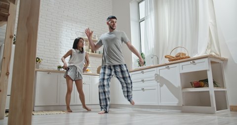Pretty interracial couple wearing pyjamas funnily dancing and singing early in morning, preparing for new day, spending time together, having fun 4k