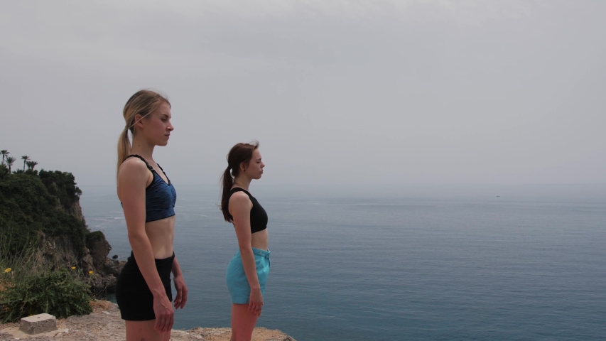 Two young woman practicing meditation in nature at high mountain cliff near the sea.